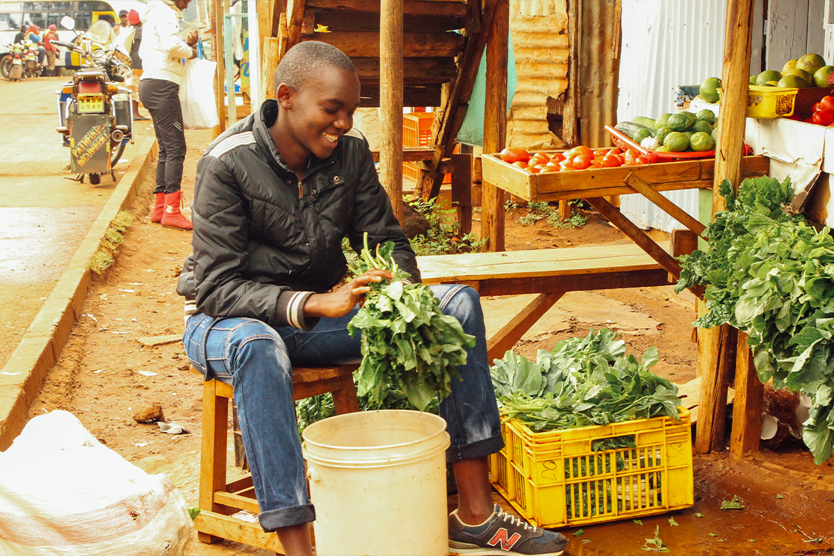 Sponsored youth Wycliff, 18, who’s also an Unbound scholarship student, cleans produce at the fruit and vegetable stand his mother operates in Nairobi, Kenya.